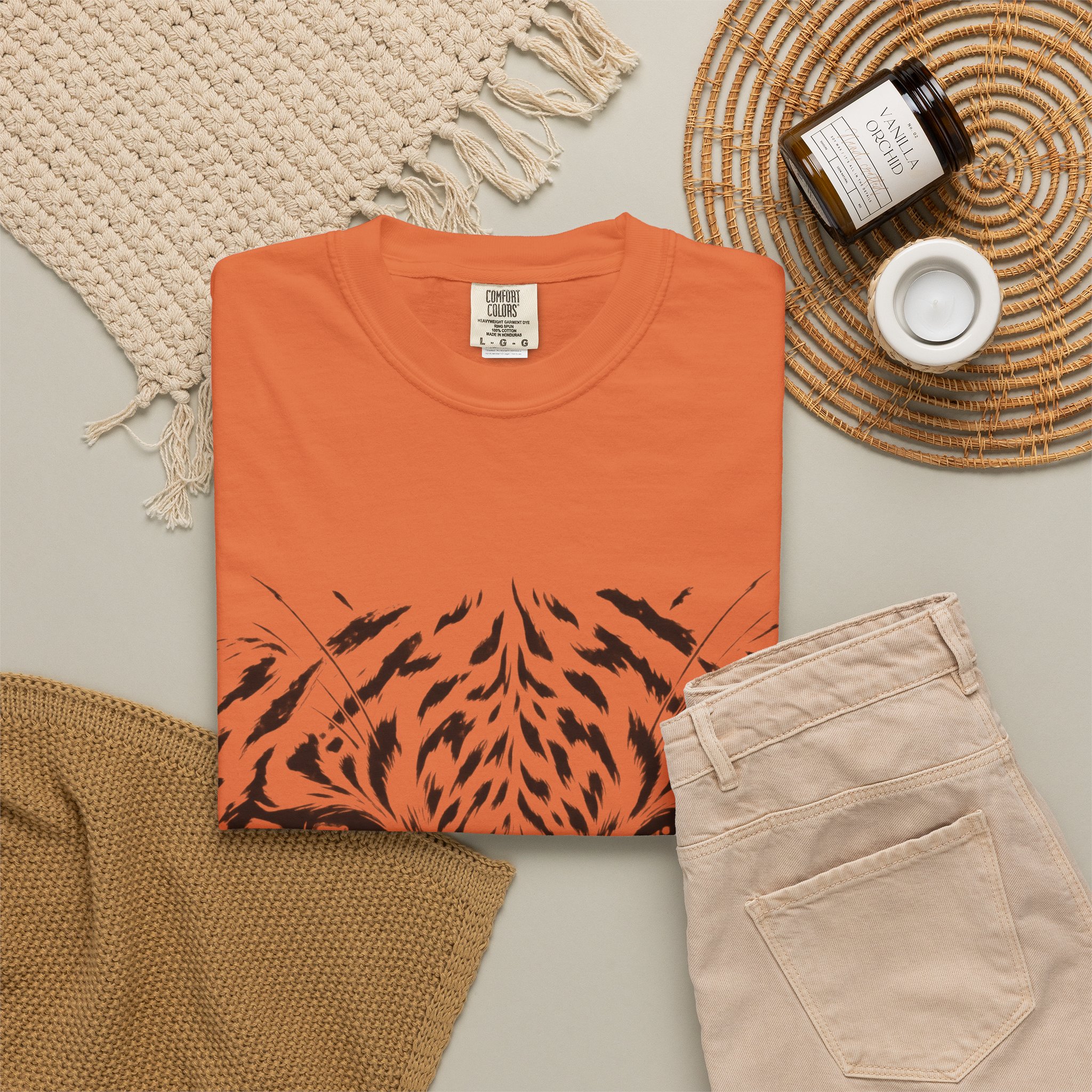 Rust-orange Tiger Face T-shirt, folded with the front design visible beside beige trousers.